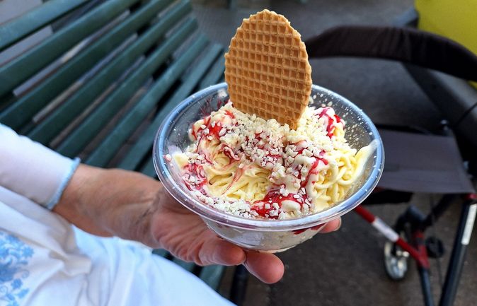 Hand hält Becher Spaghettieis mit Erdbeersoße und Waffel