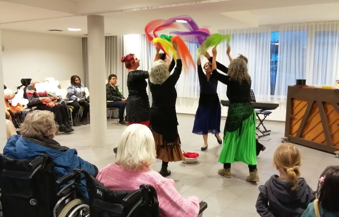 Tänzerinnen schwingen bunte Tücher vor älterem Publikum