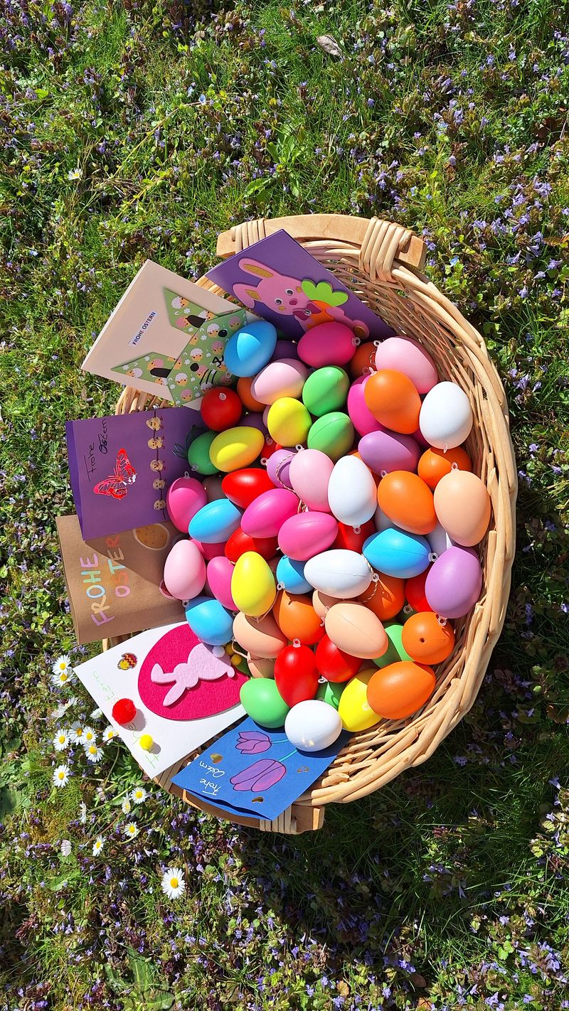 Weidenkorb mit bunten Ostereiern und Kinderbastelkarten im Gras