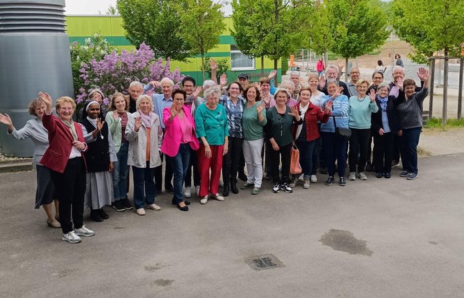 Gruppe Ehrenamtlicher winkt vor grünem Gebäude und Flieder