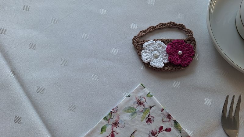 Tisch mit gehäkeltem Körbchen mit Frühlingsblüten und Serviette