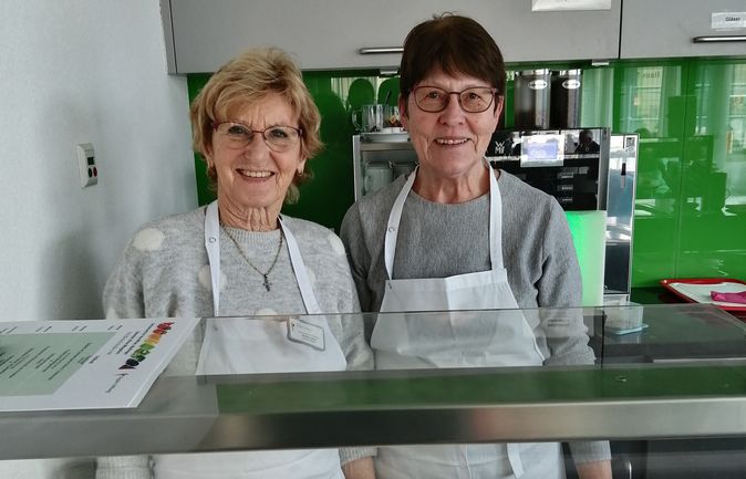 Zwei Frauen mit Schürzen hinter Cafétheke mit Kuchen