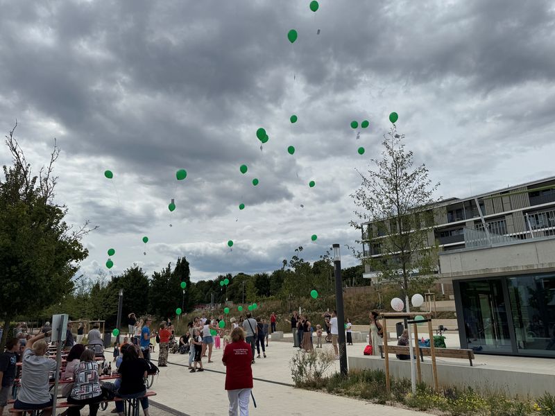 Menschen aller Generationen lassen grüne Luftballons in den Himmel steigen