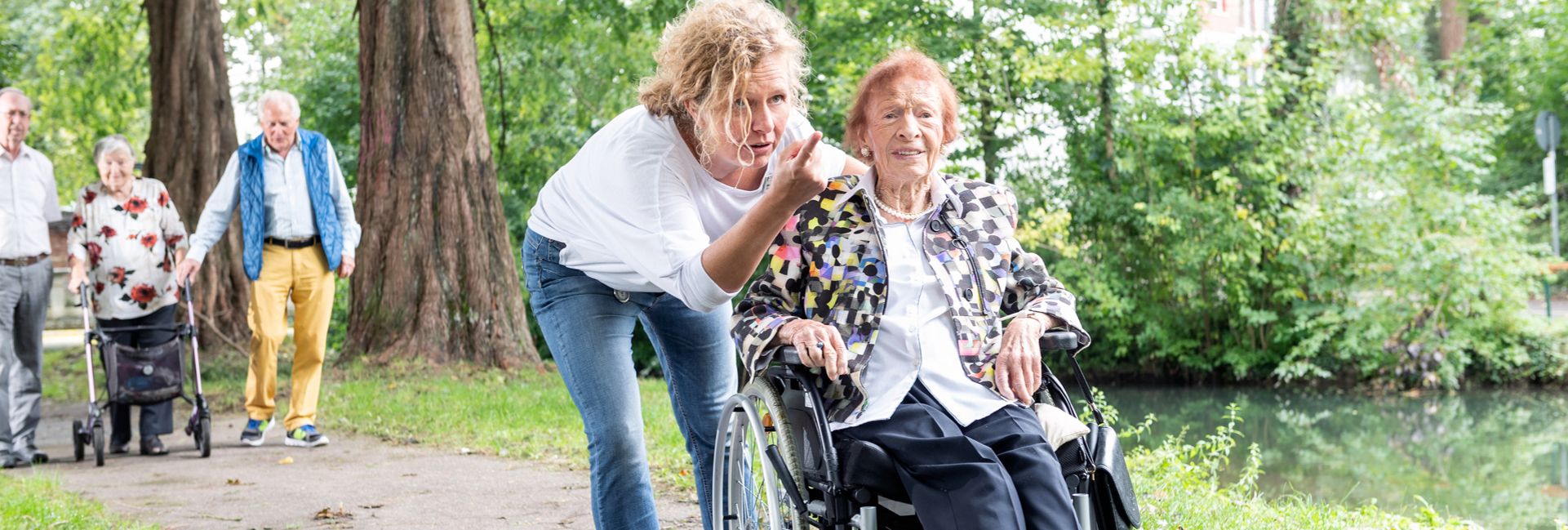 Pflegekraft zeigt der älteren Frau im Rollstuhl etwas im Park